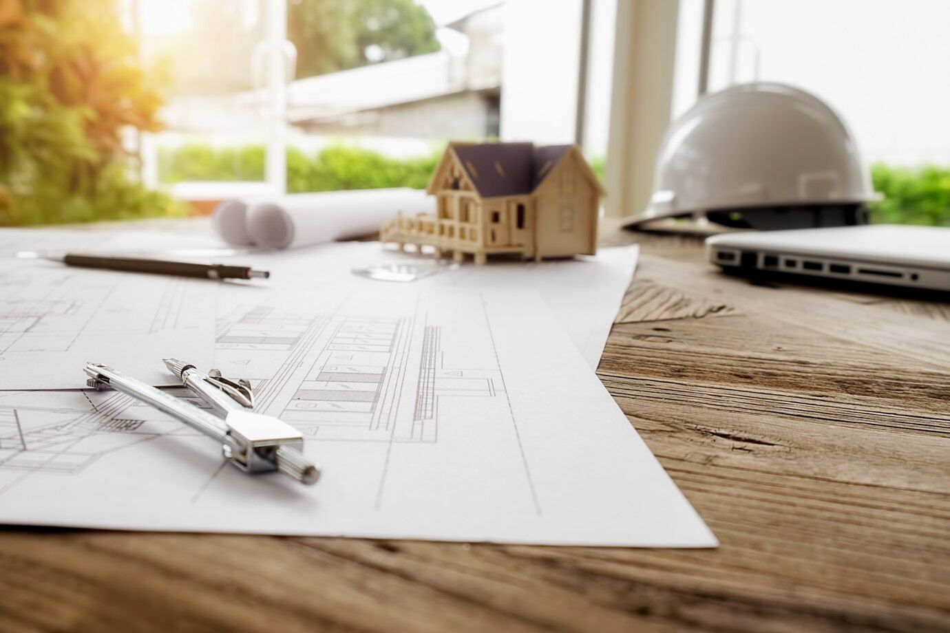 Architectural blueprints, model home, and hard hat on a planning desk